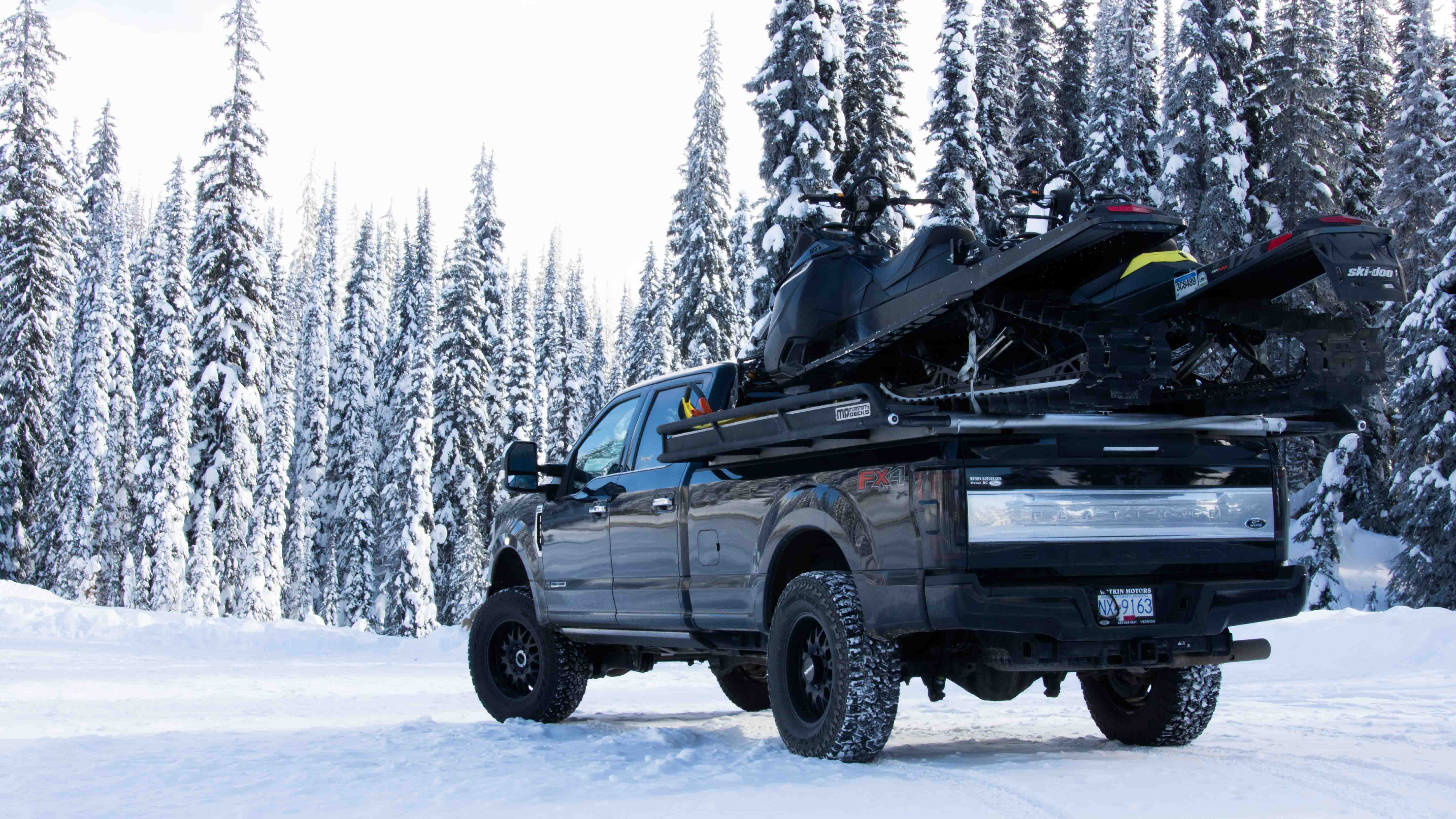 Ford F350 Platinum Full sized pickup truck with 8-foot aluminum sled deck moving two snowmobiles 